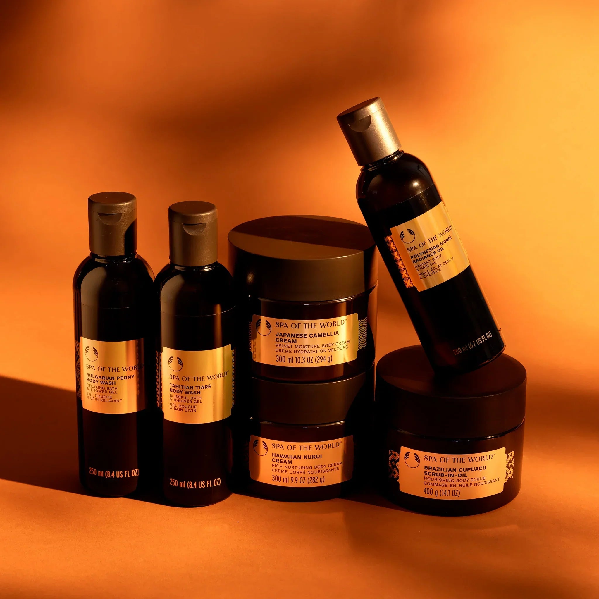 Collection of The Body Shop's Spa of the World products including body washes, creams, and oils on a shadowed orange background
